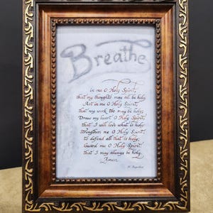 May include: A framed print with a brown wooden frame and gold accents. The print features a handwritten prayer titled "Breathe" with the text "in me O Holy Spirit, that my thoughts may all be holy. Act in me O Holy Spirit, that my work too may be holy; Draw my heart O Holy Spirit, that I will love what is holy Strengthen me o Holy Spirit, to defend all that is holy; Guard me O Holy Spirit that I may always be holy. Amen".