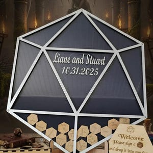 May include: A large, geometric wedding sign with the names "Liane and Stuart" and the date "10.31.2025" displayed. The sign is designed to hold small wooden tags for guests to sign. A wooden box and a welcome sign are also visible.