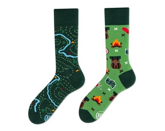 May include: A pair of green and blue socks with a camping theme. One sock features a map with a river and trees, while the other sock has a campfire, a backpack, and a compass.