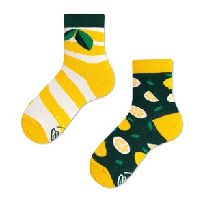 Könnte beinhalten: Ein Paar bunte Socken mit Zitronenmotiven. Eine Socke hat gelb-weiße Streifen mit grünem Bündchen, die andere hat einen dunkelgrünen Hintergrund mit Zitronenscheiben und grünen Blättern. Beide Socken haben gelbe Zehen.