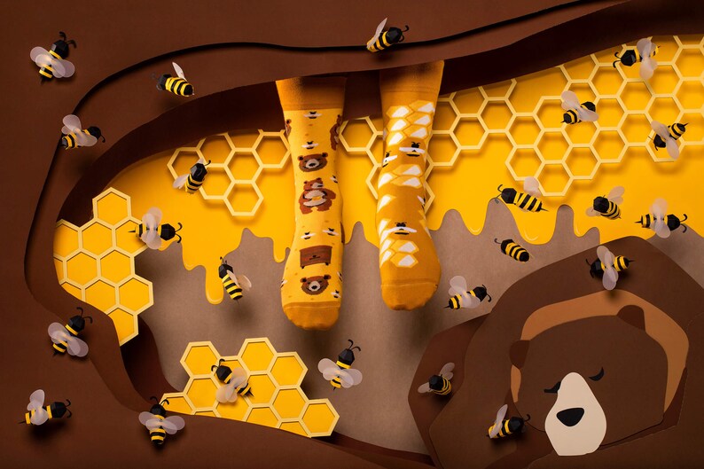 May include: A pair of yellow socks with a brown bear and honeycomb pattern. The socks are surrounded by honeycombs and bees.
