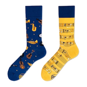 Pode incluir: Um par de meias com desenhos de instrumentos musicais. Uma meia é azul com trompete, saxofone, guitarra e violino. A outra meia é amarela com notas musicais.