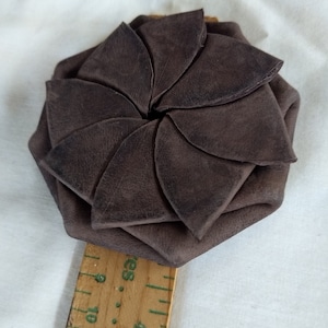 May include: A brown leather coin purse with a flower-shaped design. The purse is closed and the petals are folded inwards.