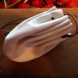 May include: A white leather pouch with a brown drawstring. The pouch is empty and folded closed.
