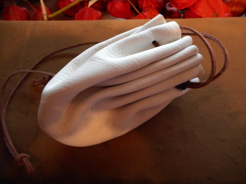 May include: A white leather pouch with a brown drawstring. The pouch is empty and folded closed.