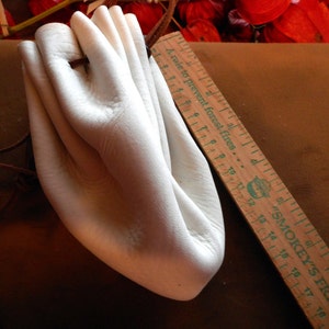 May include: White leather pouch with a drawstring closure. The pouch is folded in half and has a rustic brown leather cord attached.