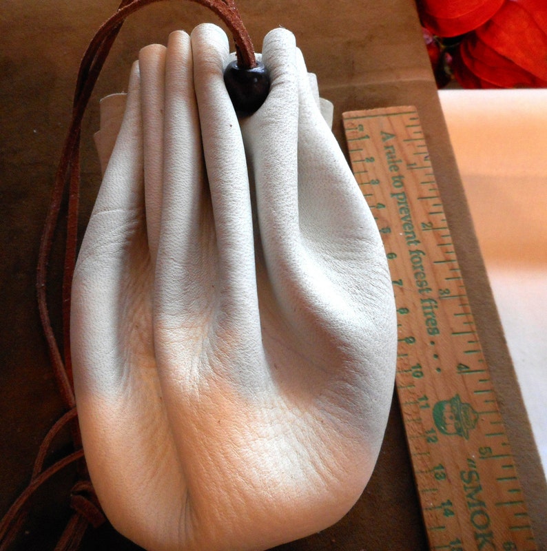 May include: A white leather drawstring pouch with a brown leather cord. The pouch is empty and has a slight sheen to it.