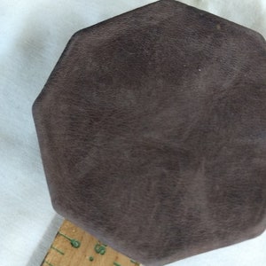 May include: A brown octagonal-shaped box with a textured surface. The box is sitting on a wooden ruler with markings in inches.