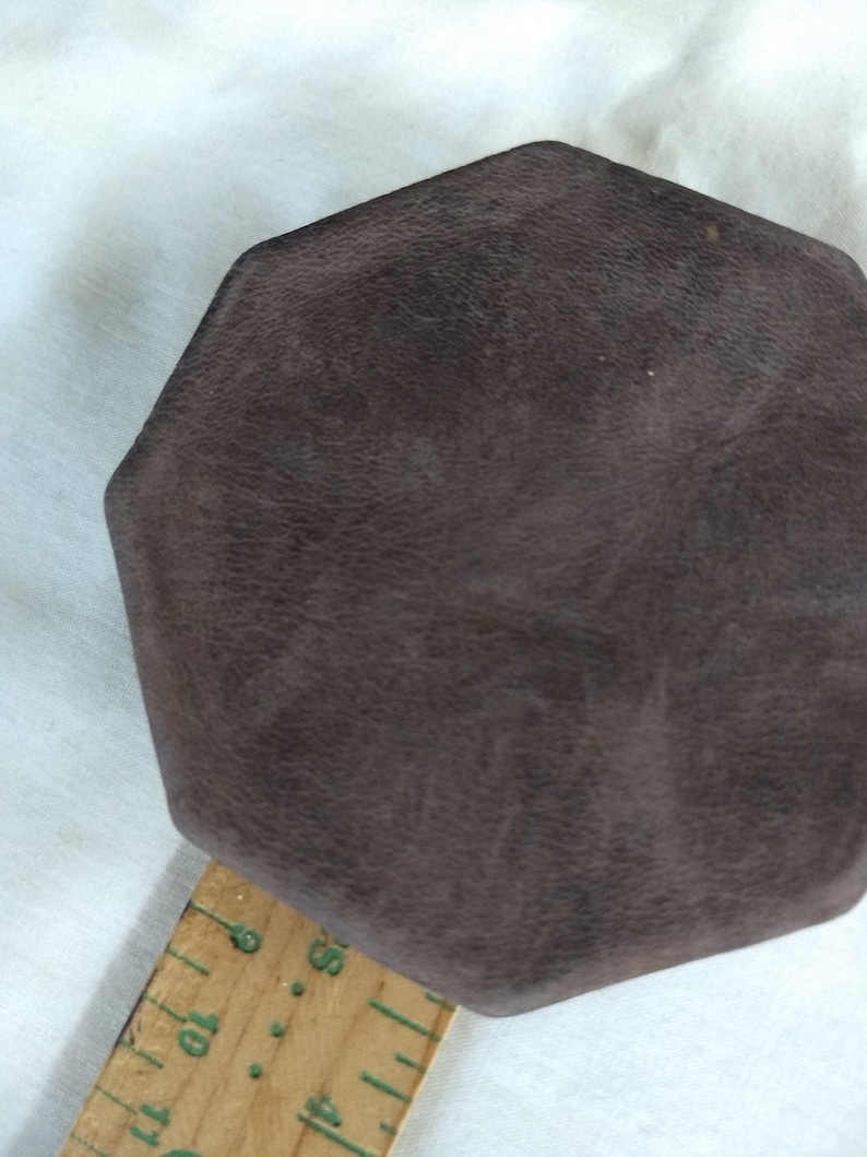 May include: A brown octagonal-shaped box with a textured surface. The box is sitting on a wooden ruler with markings in inches.