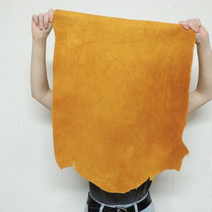 May include: A person is holding up a large piece of yellow leather in front of their face. The leather is smooth and has a slightly textured surface.