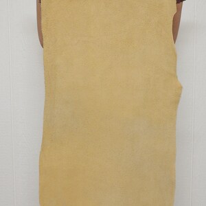May include: A large, rectangular piece of tan-colored leather with a textured surface. The leather is held up by a person, showcasing its size and shape. The edges are slightly irregular, indicating a natural cut.