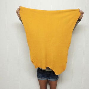 May include: A person is holding a large, bright yellow fabric in front of their body. The fabric is covering their face and torso. The person is wearing blue denim shorts.