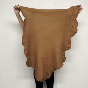 May include: A large piece of brown leather with a fringed edge. The leather is soft and supple, and it has a natural, rustic look.