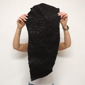 May include: A piece of black leather with a distinct, deep, and irregular wrinkled texture across its entire surface. The material is flexible and has a matte finish, showing a natural, organic pattern of raised ridges and deep crevices throughout.