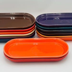 May include: A stack of oval-shaped ceramic dishes in various colors, including brown, purple, teal, orange, and red. The dishes are stacked in a staggered pattern, with the top dish being orange.