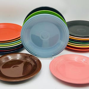 May include: A collection of colorful ceramic plates in various hues, including red, blue, green, and brown. The plates are stacked in piles and arranged on a white surface, showcasing a range of vibrant colors and designs. These plates are ideal for serving food.