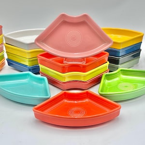 May include: A collection of colorful, ceramic Fiesta ware dishes in various shapes and colors. The dishes are stacked in neat piles, showcasing a range of hues including red, yellow, blue, green, and orange. Each dish features a concentric circle design in the center.