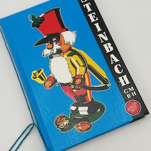May include: A blue book with a colorful illustration of a toy soldier on the cover. The book has the text "STEINBACH GMBH" and "WORLD'S BEST" on the spine.
