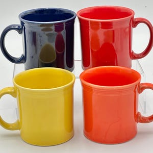 May include: Four ceramic mugs in vibrant colors: navy blue, red, yellow, and orange. Each mug has a rounded handle and a glossy finish. The mugs are arranged in a square, showcasing their bright hues and simple design.