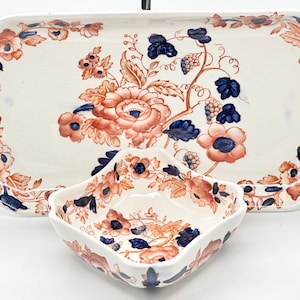 May include: A rectangular serving platter and a square bowl with a floral design. The off-white ceramic pieces feature orange and blue flowers and foliage. The platter has scalloped edges and handles.