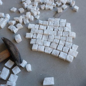May include: A collection of small, white marble blocks arranged in a pattern on a gray surface. A hammer and ruler are also present, suggesting a craft or construction project. The blocks are roughly rectangular and vary slightly in size.