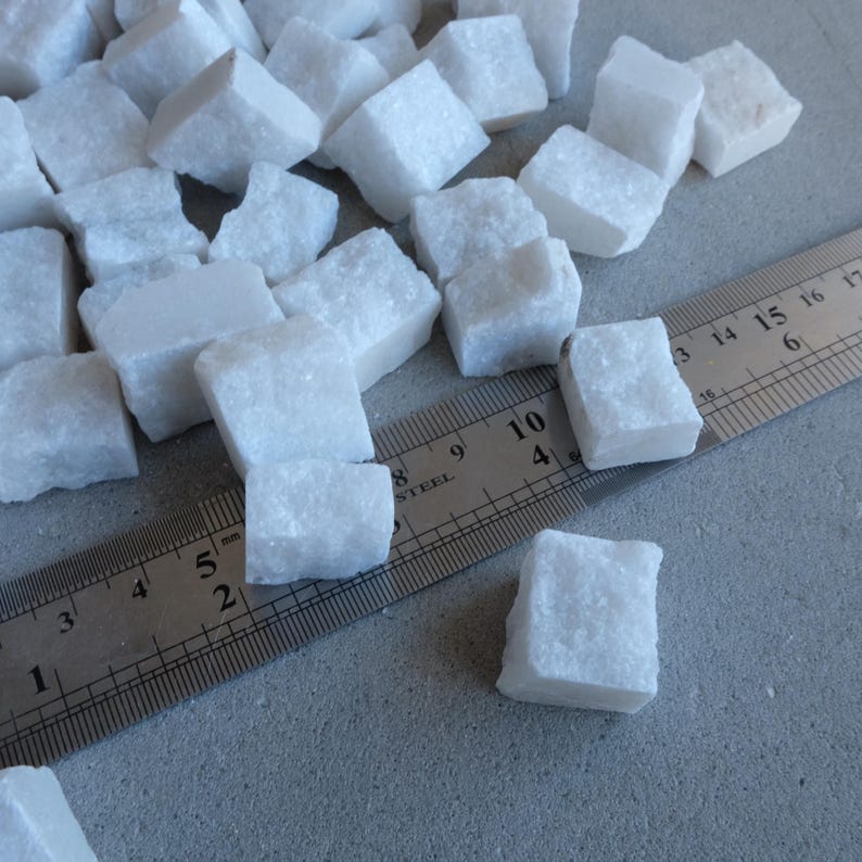 May include: A collection of small, white, irregularly shaped marble cubes. A metal ruler with inch markings is placed next to the cubes. The cubes appear to be approximately 0.75 inches in size.