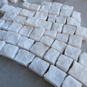 May include: A collection of small, irregularly shaped white stone blocks arranged closely together. The blocks have a rough, textured surface and vary slightly in size and shape. The overall arrangement suggests a mosaic or building material.