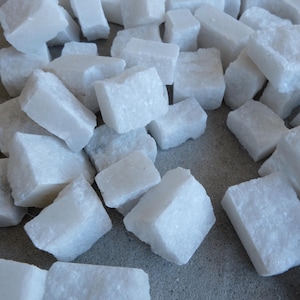 May include: A collection of irregularly shaped, white, rough-textured stones. The stones are scattered across a neutral-toned surface, with varying sizes and angles. The overall impression is of a natural, raw material.