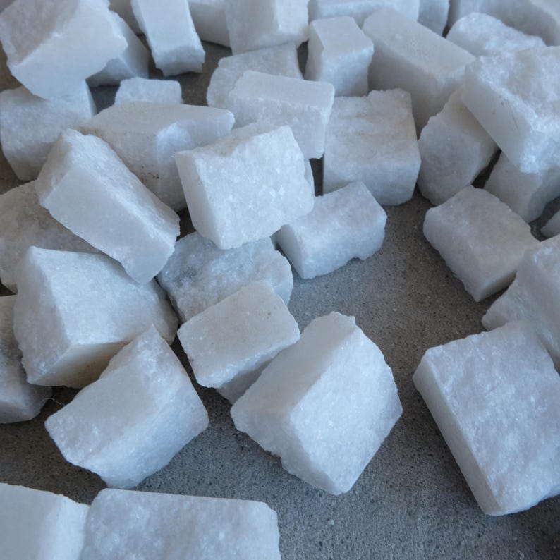 May include: A collection of irregularly shaped, white, rough-textured stones. The stones are scattered across a neutral-toned surface, with varying sizes and angles. The overall impression is of a natural, raw material.