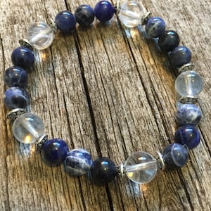 May include: A blue and clear crystal beaded bracelet with silver accents. The bracelet is made with round beads and is strung on elastic.