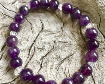 May include: A purple amethyst and clear crystal beaded bracelet. The bracelet is made with round beads and is strung on elastic.