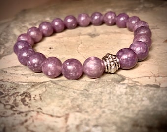 May include: A purple gemstone bracelet with a silver bead accent. The bracelet is made of round beads and is approximately 7 inches in length.
