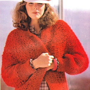 May include: A red crocheted cardigan with a loose fit and a V-neck. The cardigan is worn over a plaid shirt. The text "CROCHET" is visible in the bottom right corner of the image.