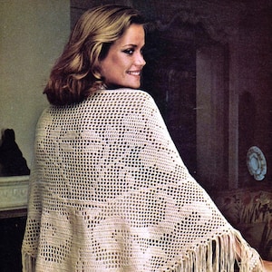 Può includere: Uno scialle bianco all'uncinetto con un delicato motivo traforato e bordi a frangia. Lo scialle è drappeggiato sulle spalle di una donna.
