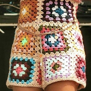 May include: A colorful crochet top and shorts set. The garment features a patchwork design with squares in various colors, including blue, green, orange, and pink. A gold chain belt accents the waist, adding a touch of elegance to the bohemian style.