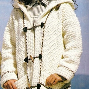 May include: A white crocheted hooded cardigan with brown trim and toggle closures. The cardigan has pockets on the front and a striped shirt underneath.