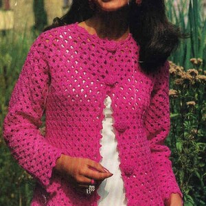 Può includere: Un cardigan all'uncinetto rosa acceso, aperto sul davanti, con maniche lunghe. Il cardigan ha un bordo smerlato e viene indossato sopra un capo bianco. L'immagine è una fotografia in stile vintage.