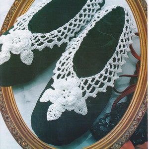 May include: A pair of black velvet slippers with white crocheted trim and a flower design. The slippers are displayed in a gold oval frame.
