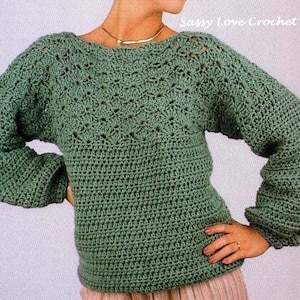 May include: A green crocheted sweater with a lacy pattern on the yoke and sleeves. The sweater has a boat neck and a relaxed fit.
