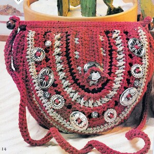 Puede incluir: Un bolso de crochet rojo y blanco con una correa larga y botones de metal plateado. El bolso está sobre una superficie blanca.