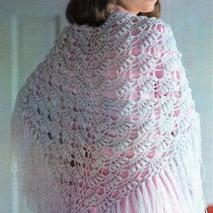 Puede incluir: Un chal de ganchillo blanco con flecos, que presenta un delicado patrón de calado. El chal se lleva sobre una blusa rosa.