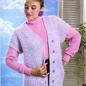 May include: A purple and pink crocheted vest with a pink turtleneck underneath and purple buttons. The model is wearing a black skirt.