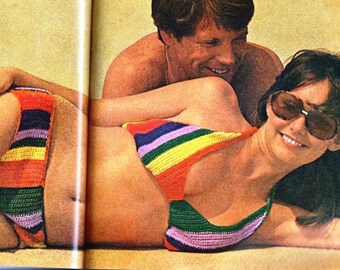 Könnte beinhalten: Ein Paar am Strand, das farbenfrohe gehäkelte Badebekleidung trägt. Die Frau trägt ein regenbogenfarbenes gestreiftes Bikinioberteil und ein passendes Unterteil. Der Mann trägt ein weißes Hemd.