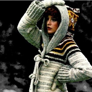 Könnte beinhalten: Ein gehäkelter Kapuzenpullover mit einem gestreiften Muster in Braun-, Weiß- und Gelbtönen. Der Pullover hat einen Bindegürtel in der Taille und eine Kapuze mit einem gehäkelten Design.