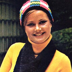 May include: A woman wearing a yellow turtleneck sweater with a black scarf and a colorful crocheted hat.