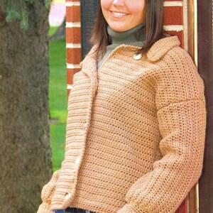 May include: A brown crocheted button-up sweater with a mock neck. The sweater is worn by a person standing next to a brick wall. "Everyone adores button-up sweaters. Here is one that is warm enough to be a jacket. This is first-rate, back-to-school apparel!"
