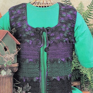 Op de afbeelding: Een gebreid vest met een strik sluiting. Het vest is zwart en groen met paarse accenten. Het vest is op een mannequin die een groen shirt draagt.