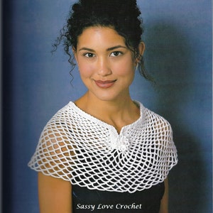 May include: A white, open-weave crochet shawl with a scalloped edge. The shawl is worn over a black top. The text "Sassy Love Crochet" is visible at the bottom of the image.