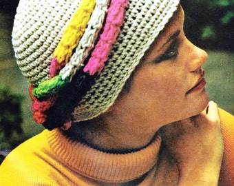 May include: A white crocheted hat with a colorful crocheted band. The band is made of pink, yellow, and green yarn. The hat is worn by a person with a yellow turtleneck sweater.