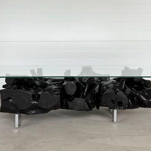 May include: A black coffee table made from a large, natural tree root with a glass top. The table has four silver metal legs.